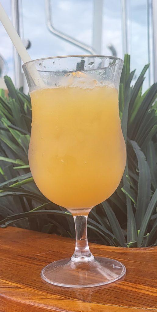 A Painkiller cocktail in a hurricane glass with some plants behind it.